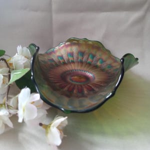 May include: An iridescent glass bowl with a scalloped rim. The bowl features a blend of colors, including green, gold, and purple, creating a shimmering effect. The bowl's design is reminiscent of a flower, with a central pattern radiating outwards.