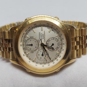 May include: A gold Citizen Quartz Alarm Chronograph watch with a white face and black hands. The watch has a tachymeter scale around the outer edge of the face. The watch also has a calendar, alarm, and chronograph functions.