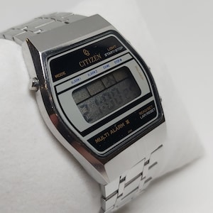 May include: A silver Citizen Multi Alarm II digital watch with a black face and a silver metal strap. The watch has a range of functions, including alarm, stopwatch, and timer.