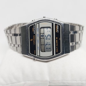 May include: A silver Citizen Multi Alarm III watch with a black face and a digital display. The watch has a silver metal strap and features buttons for light, start/stop, alarm, and lap/reset.
