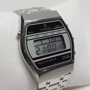May include: A silver Citizen Multi Alarm III digital watch with a black face and a silver metal strap. The watch has a digital display showing the time as 2:00. The watch has buttons for mode, alarm 1, alarm 2, chime, stop/w, light, start/stop, read/set, and lap/reset.