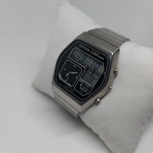May include: A silver Citizen Digi-Ana watch with a black face and a digital display. The watch features a chronograph, alarm, and chime functions. The watch is on a silver metal band.
