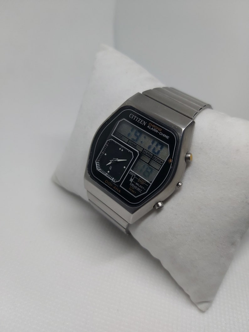 May include: A silver Citizen Digi-Ana watch with a black face and a digital display. The watch features a chronograph, alarm, and chime functions. The watch is on a silver metal band.