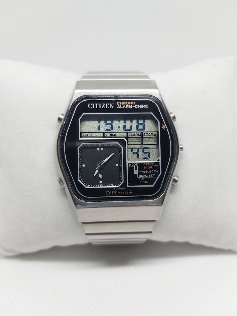 May include: A silver Citizen watch with a black face and a digital display. The watch has a chronograph, alarm, and chime functions. The display shows the time as 7:08 and the date as 45. The watch also has a small analog dial.