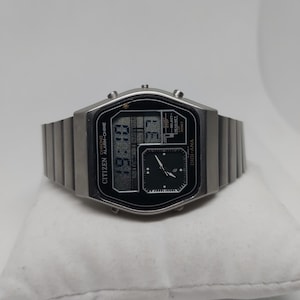 May include: A silver Citizen Digi-Ana watch with a black face and a silver metal band. The watch has a digital display showing the time and a smaller analog display with hands.