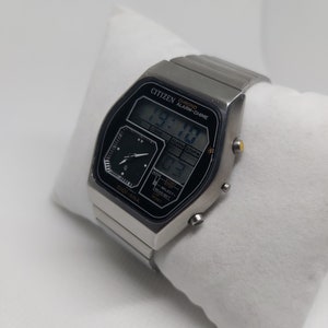 May include: A silver Citizen Digi-Ana watch with a black face and digital display. The watch features a chronograph, alarm, and chime functions. The watch face displays the time, date, and alarm settings.