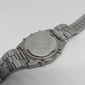 May include: A silver Citizen watch with a stainless steel band. The watch face is not visible, but the back of the watch has the Citizen logo and model number.