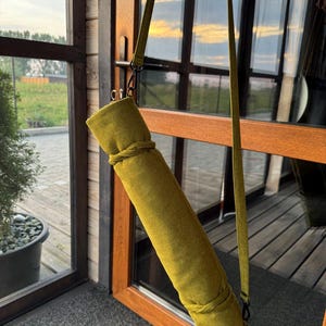 May include: A green yoga mat carrier with a long adjustable strap. The carrier is made of a textured fabric and has a zipper closure.