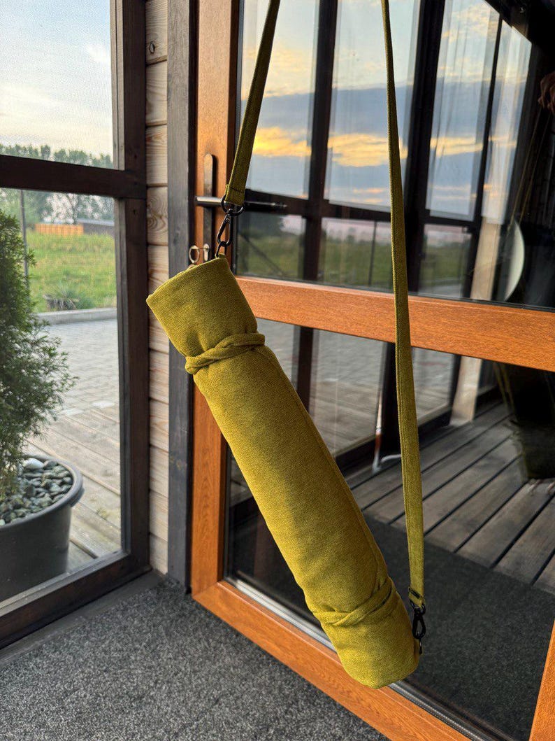May include: A green yoga mat carrier with a long adjustable strap. The carrier is made of a textured fabric and has a zipper closure.