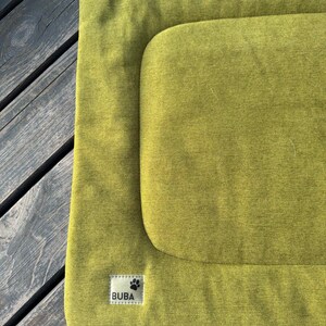 May include: A green dog bed with a raised edge and a label that says "BUBA" with a paw print.