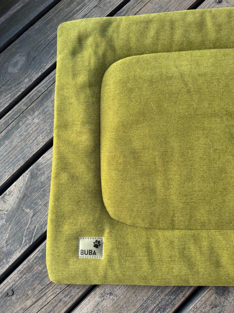 May include: A green dog bed with a raised edge and a label that says "BUBA" with a paw print.