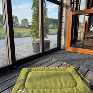 May include: A green rectangular dog bed with a brown border and the word "BUBA" printed on the bottom left corner. The bed is on a wooden floor.