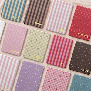 May include: A collection of rectangular cases featuring various patterns including vertical stripes, anchors, stars, and hearts in colors like blue, brown, pink, red, and purple. Each case is personalized with gold text including names and initials.
