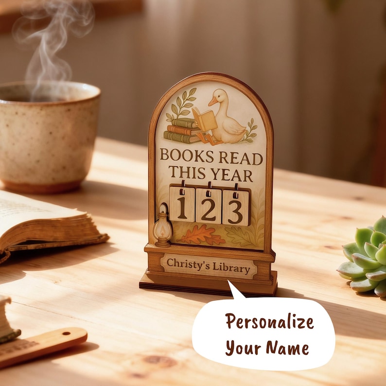 May include: Wooden desk calendar with a duck reading a book illustration. The text reads "BOOKS READ THIS YEAR" with the numbers "123" displayed. The bottom of the calendar reads "Christy's Library". A speech bubble says "Personalize Your Name".