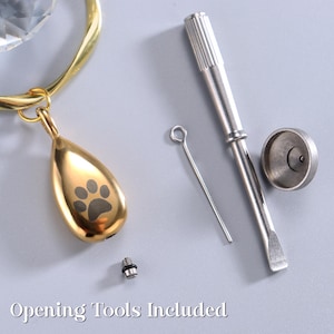 May include: A gold-colored teardrop-shaped pendant with a paw print design, a gold-colored ring, and opening tools. The text "Opening Tools Included" is at the bottom of the image.