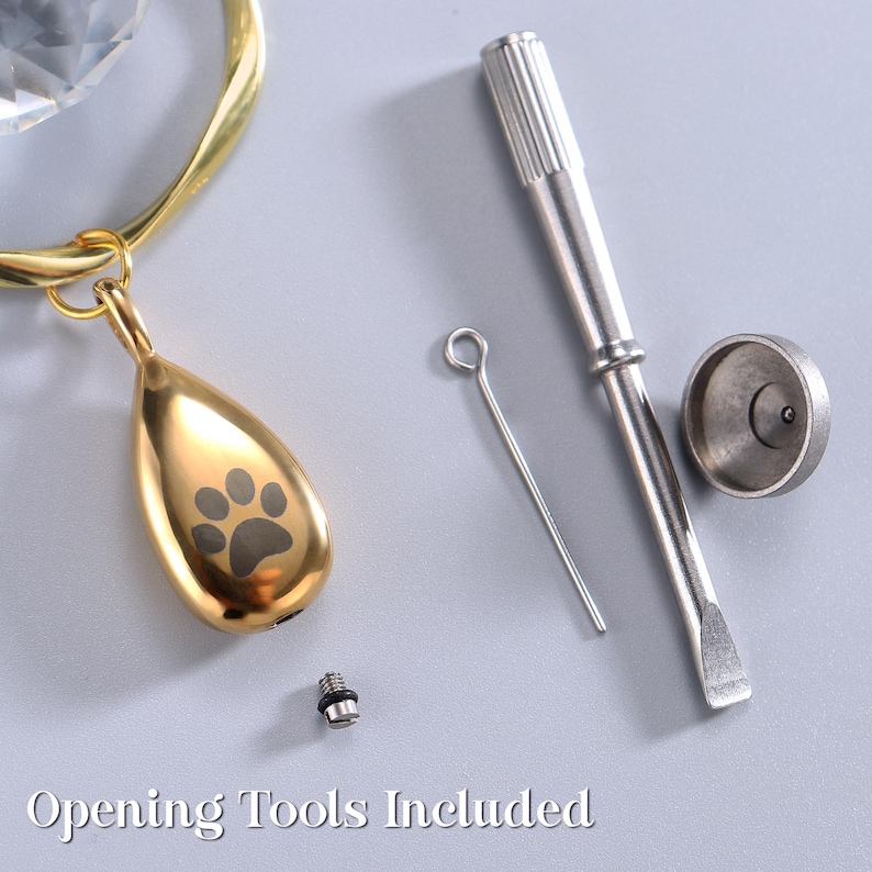 May include: A gold-colored teardrop-shaped pendant with a paw print design, a gold-colored ring, and opening tools. The text "Opening Tools Included" is at the bottom of the image.