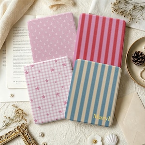 May include: Four rectangular e-reader cases with distinct patterns: one light pink with white anchors, one with red and pink vertical stripes, one with a pink gingham pattern featuring small stars, and one with blue and beige stripes labeled with the name Maryl.