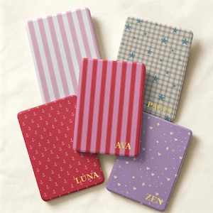 May include: Five rectangular cases with rounded corners. One has pink and white stripes, one has blue stars on a plaid background with the name PAGE, one has red and pink stripes with the name AVA, one has red anchors with the name LUNA, and one has purple hearts and stars with the name ZEN.