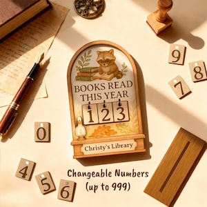 May include: A wooden book counter with a raccoon wearing glasses reading a book. The counter reads "BOOKS READ THIS YEAR" with changeable numbers. Includes additional wooden number tiles from 0 to 9. The counter is labeled "Christy's Library".