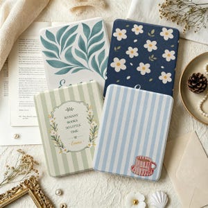 May include: Four rectangular e-reader cases with distinct designs: one with green leaves, one with white flowers on navy blue, one with green stripes and the text "SO MANY BOOKS SO LITTLE TIME - Emma", and one with blue stripes and a red teacup.