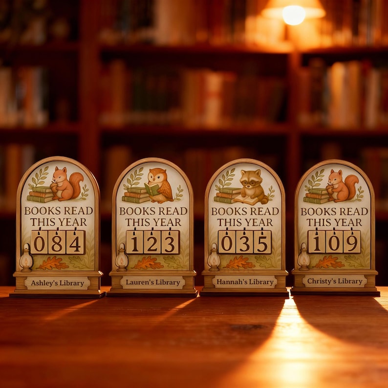May include: Four wooden book counters with different numbers displayed. Each counter has a different animal illustration at the top, including a squirrel, owl, and raccoon. The text "BOOKS READ THIS YEAR" is above the numbers, and each counter has a name at the bottom.