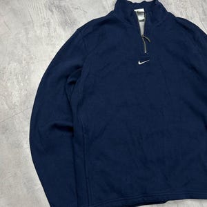 K&ouml;nnte beinhalten: Marineblaues Langarm-Pullover-Sweatshirt mit Viertelrei&szlig;verschluss und kleinem wei&szlig;em Nike-Logo auf der Brust. Der Kragen ist im Stehkragen-Stil. Das Sweatshirt hat eine lockere Passform.