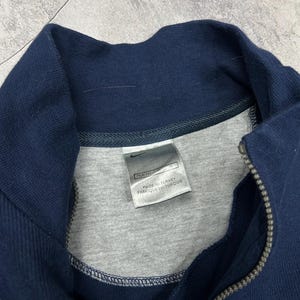 K&ouml;nnte beinhalten: Marineblaues Sweatshirt mit Rei&szlig;verschluss, grauem Innenfutter und hohem Kragen. Der Rei&szlig;verschluss ist silberfarben. Das Etikett lautet "MADE IN TURKEY" und "FABRIQUE EN TURQUIE".