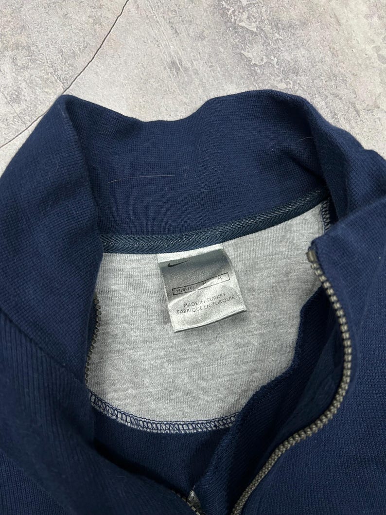 K&ouml;nnte beinhalten: Marineblaues Sweatshirt mit Rei&szlig;verschluss, grauem Innenfutter und hohem Kragen. Der Rei&szlig;verschluss ist silberfarben. Das Etikett lautet "MADE IN TURKEY" und "FABRIQUE EN TURQUIE".