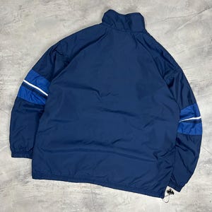 Op de afbeelding: Marineblau sportjack met een hoge kraag en een trekkoord aan de zoom. De jas heeft blauwe en witte strepen op de mouwen. De jas is gemaakt van een lichtgewicht materiaal.