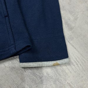 K&ouml;nnte beinhalten: Nahaufnahme eines marineblauen Sweatshirt-&Auml;rmels. Das B&uuml;ndchen hat einen grauen Besatz mit einem braunen Fleck. Der Stoff scheint ein dickes Strickmaterial zu sein.