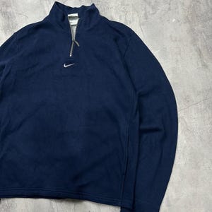K&ouml;nnte beinhalten: Marineblaues Langarm-Pullover mit Stehkragen und silbernem Rei&szlig;verschluss. Mit kleinem wei&szlig;em Nike-Logo auf der Brust. Die Manschetten und der Kragen haben einen wei&szlig;en Besatz.