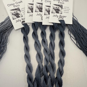 May include: Several skeins of Otter Creek Floss in a dark gray color, labeled "Jolly Roger." Each skein is 10 yards of 6-strand, 100% cotton floss. The labels feature a small illustration of an otter.