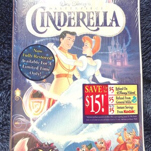 May include: A sealed VHS tape of Disney's animated film, Cinderella. The cover features Cinderella and Prince Charming dancing, with a castle in the background. The tape has a promotional sticker offering savings.