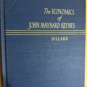 May include: A dark blue hardcover book titled The Economics of John Maynard Keynes by Dillard. The front cover features gold embossed lettering and two horizontal gold lines separating the title from the author's name on the textured fabric cover.