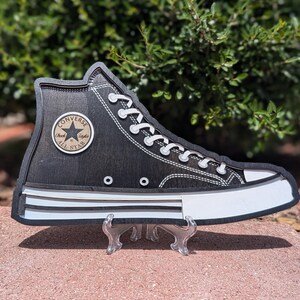 May include: Black Converse Chuck Taylor All Star high-top trainer with white laces and a white sole. The shoe is made of canvas and has a black star logo on the side.