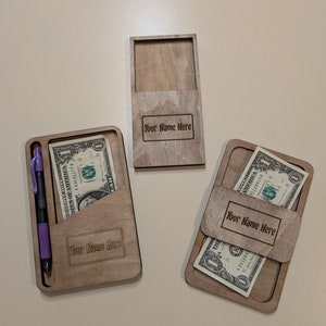 Puede incluir: Tres cajas de madera con ranuras para efectivo y un bolígrafo. Las cajas están grabadas con el texto "Your Name Here".