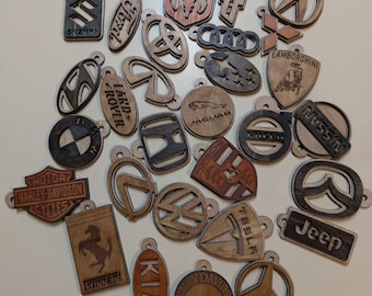 May include: A collection of wooden keyrings featuring various car logos, including Dodge, Chevrolet, Lamborghini, Jaguar, Nissan, Jeep, Harley-Davidson, Ferrari, and Kia.