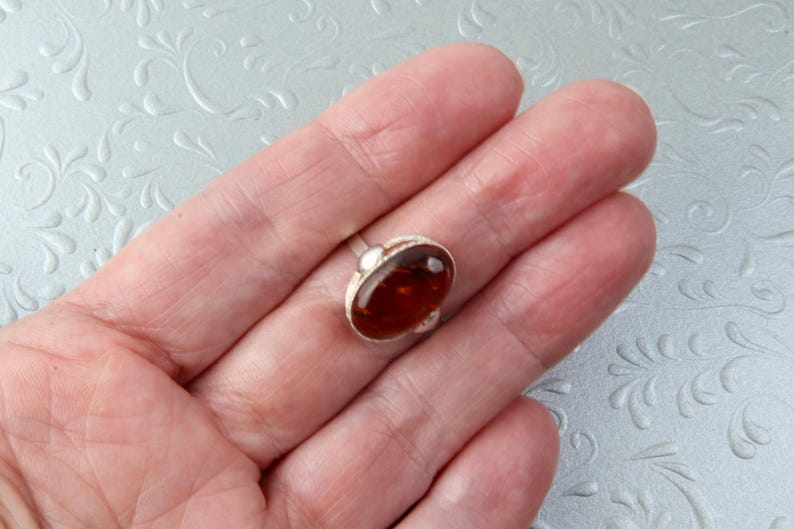 Puede incluir: Un anillo de plata con una piedra de &aacute;mbar ovalada grande.