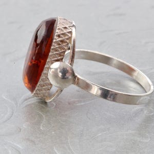 Puede incluir: Un anillo de plata con una gran piedra preciosa ovalada de &aacute;mbar. El anillo tiene una banda texturizada y un engaste redondo y liso para la piedra.
