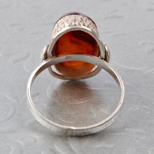 Puede incluir: Un anillo de plata con una piedra de &aacute;mbar grande de forma ovalada engastada en un engaste decorativo. El anillo se muestra desde atr&aacute;s, revelando la banda lisa.