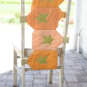 Peut inclure: Une chaise peinte en blanc avec un dossier en tissu orange, pêche et vert à motifs d'étoiles. La chaise est sur un patio en briques.