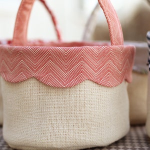 Może przedstawiać: Trzy koszyczki wielkanocne z tkaniny z różnymi wzorzystymi lamówkami. Koszyczki są wykonane z naturalnego materiału jutowego i mają czerwone, białe i czarne lamówki.