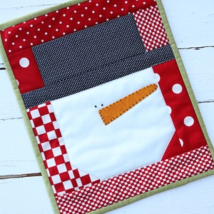 May include: A handmade quilted snowman wall hanging with red and white polka dot fabric, black and white gingham fabric, and red and white checkered fabric. The snowman has a white felt face with a carrot nose and black eyes.