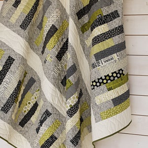 May include: A quilt with a geometric pattern of black, white, and green stripes. The quilt is hanging on a white wall.