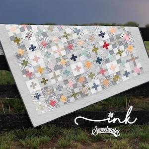 May include: A quilt featuring a grid pattern of small squares and cross shapes in various colors including red, yellow, pink, green, and blue, interspersed with grey and white patterned squares. The text "ink Sweetwater" is printed in white.