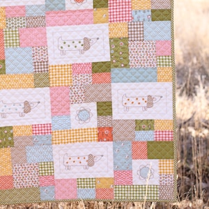 May include: A patchwork quilt with a repeating pattern of dachshund dog illustrations. The quilt uses various fabric patterns in pink, green, yellow, and blue. The quilt's border is a light green.