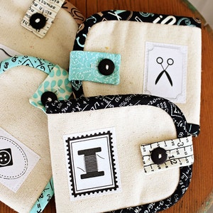 Pu&ograve; includere: Quattro piccole pochette in tessuto con diversi design. Ogni pochette ha uno sfondo bianco con una grafica in bianco e nero sul davanti. Le grafiche includono un bottone, un rocchetto di filo, un paio di forbici e un righello. Le pochette sono rifinite con tessuto bianco e nero.