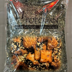 May include: A clear plastic bag filled with dark green seaweed and small, crispy, brown snacks. The bag has a label that reads "INKI POPCORN Seasoned Seaweed".