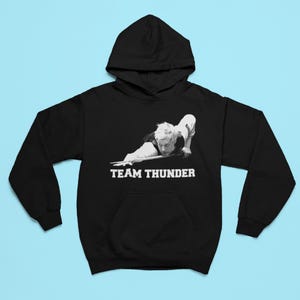 Puede incluir: Sudadera con capucha negra con un gráfico blanco de una persona jugando al billar y el texto "TEAM THUNDER".
