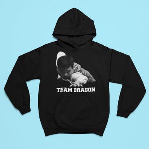 Puede incluir: Sudadera con capucha negra con un gráfico blanco de una persona jugando al billar con el texto "TEAM DRAGON" impreso debajo.